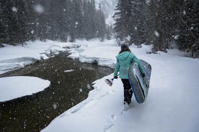Rear view of woman carrying paddleboard while walking on snowfield