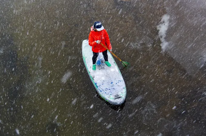 High angle view of woman paddleboarding on river during snowfall