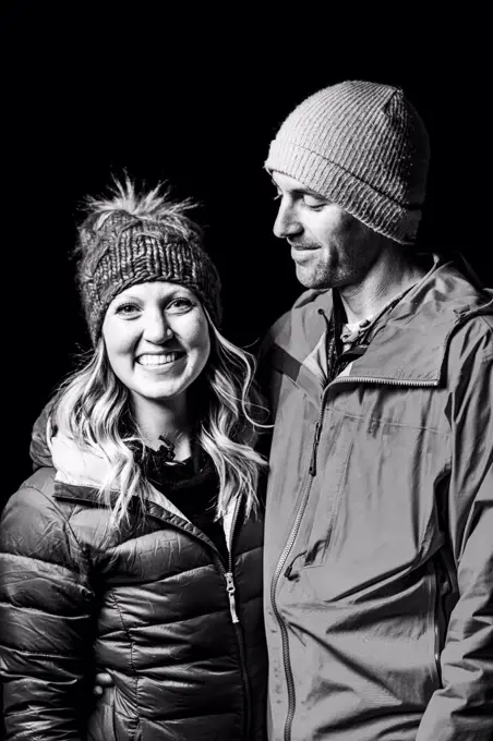Smiling couple in warm clothing standing against black background