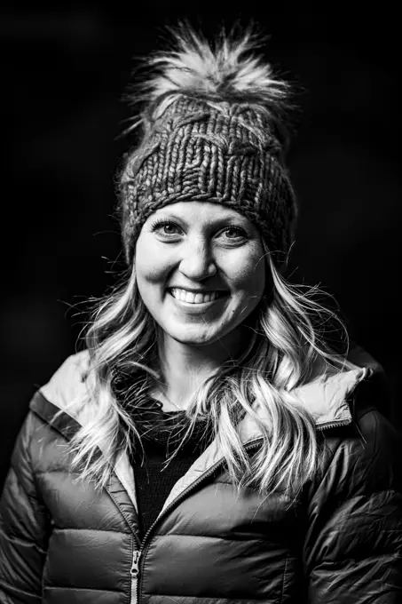 Portrait of smiling young woman in warm clothing against black background
