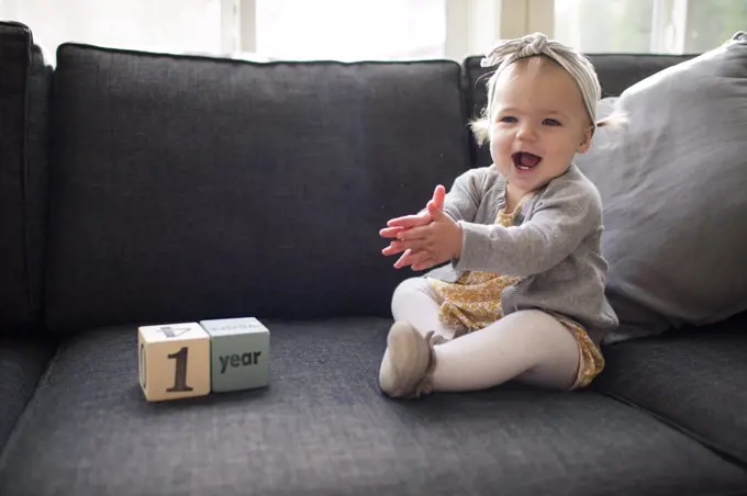 One year old girl sitting on couch clapping with excitement