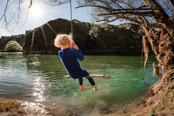Blonde child on swing over river in New Zealand on sunny day