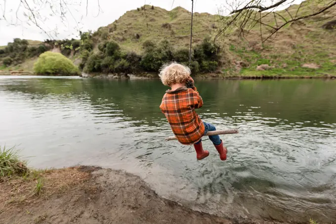 Small curly haired child swinging near river