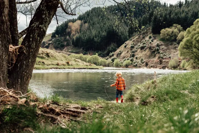 Little curly haired kid exploring river bank in boots