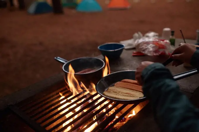 unrecognizable person preparing dinner at the campfire near his tent