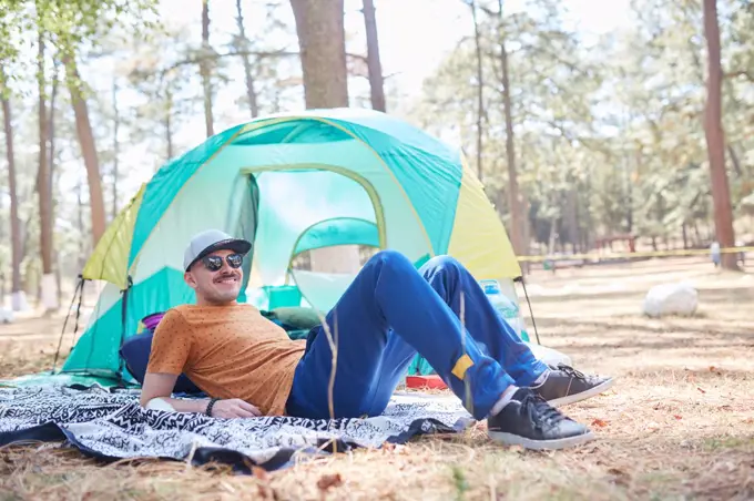 smiling young man with sunglasses lying outside his tent