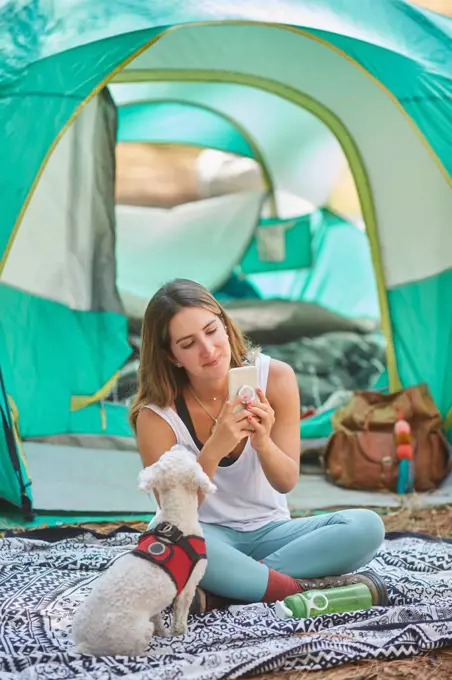 woman using her smartphone in the company of her dog outside her tent