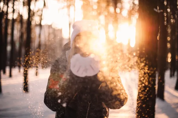 Woman blowing snow standing in park at sunset during winter