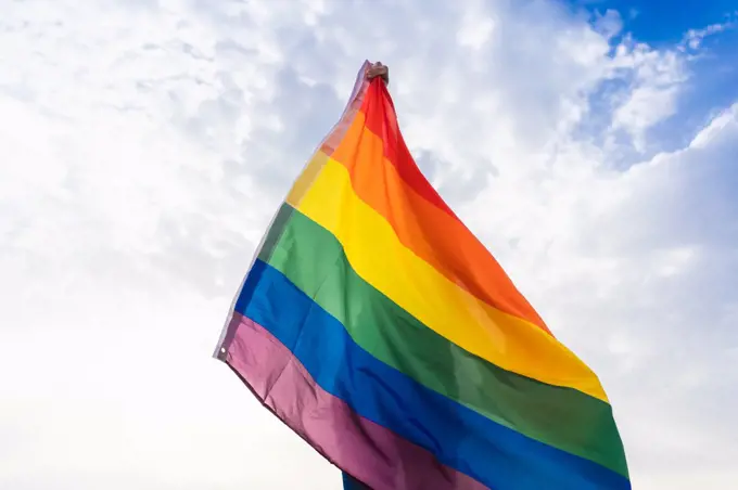 Unknown person posing with LGBT flag covering his body with sky behind