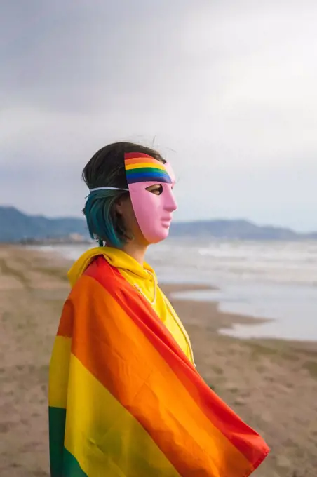 Masked person with pink mask with LGBT rainbow flag on the beach
