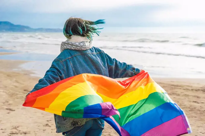 Woman running with colorful LGBT flag waving on the beach