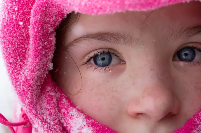 A close up of a girl Dressed for Winter with snowflakes in her eyelashes