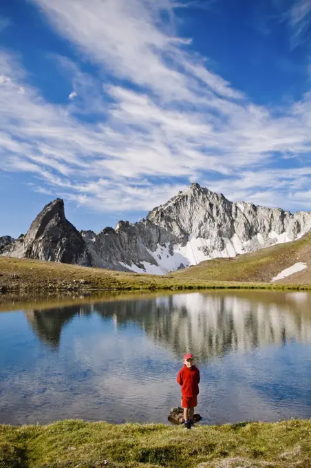 Young boy wearing red, standing in front of alpine lake, scenic peaks
