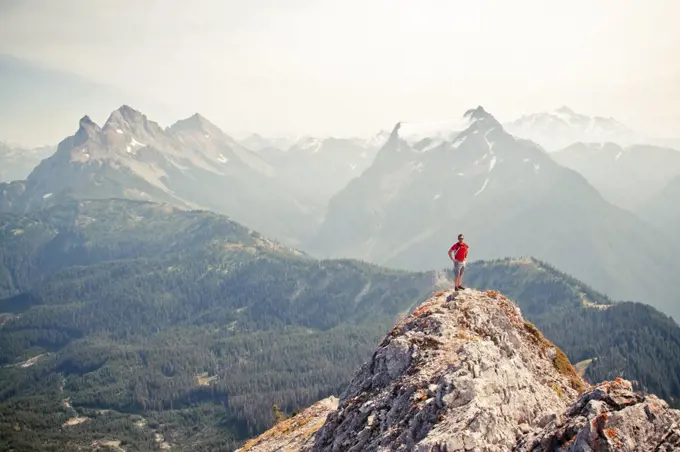 Trail runner stands on the airy summit of a rocky mountain ridge.