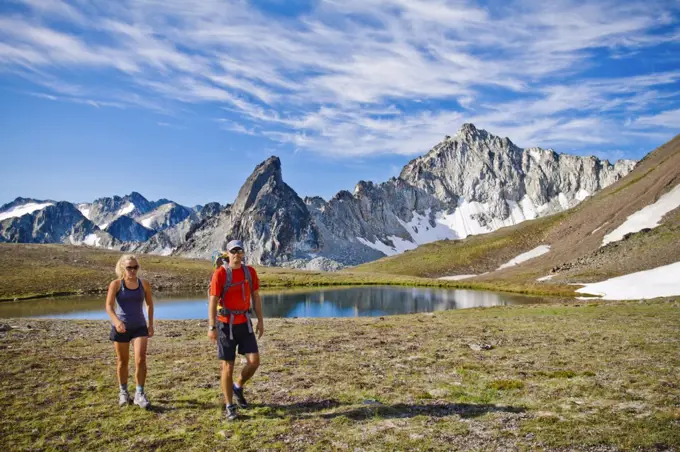 couple backpacking in scenic alpine meadow, mountains behind.