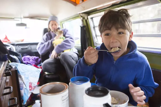 An 8 year-old boy eats oatmeal in VW camper van during family roadtrip