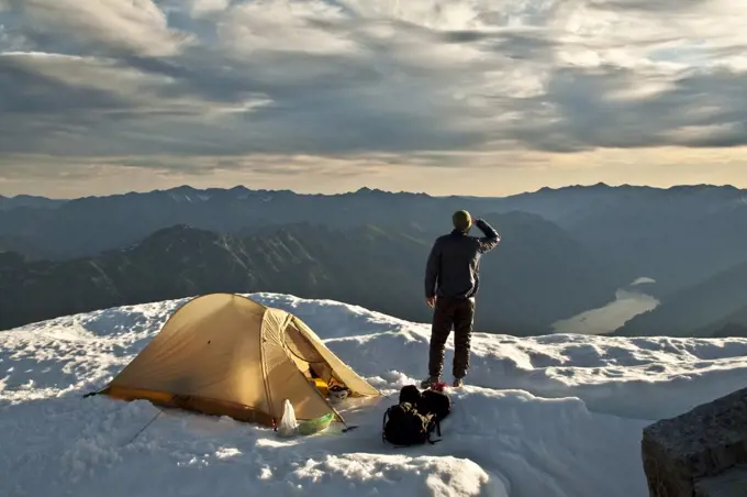 Hiker stands next to tent on mountain summit, Whistler, B.C. Canada.
