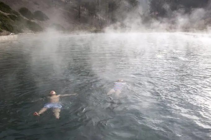 Two children float in a Trinity Hot Springs pool with steam rising