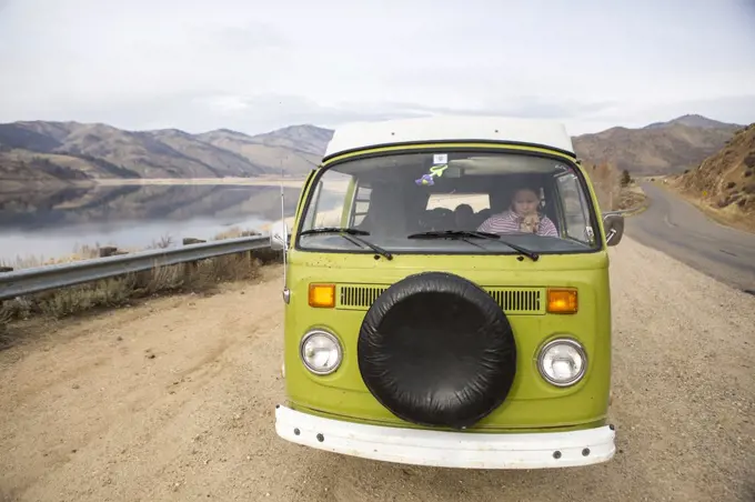 A woman and her dog are visible through windshield of VW camper van