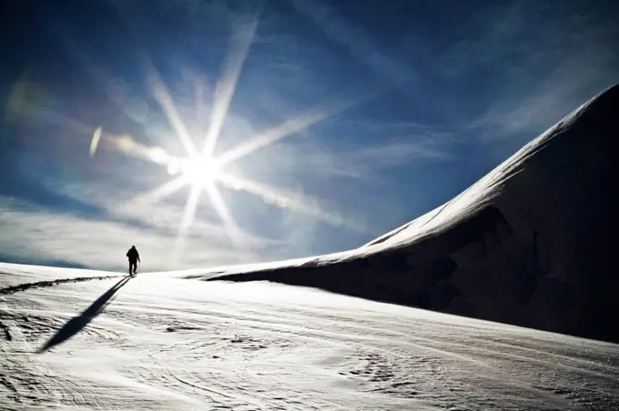 Rear view of silhouetted person ski touring towards snowy mountain.