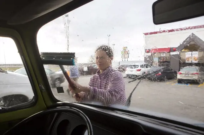 A woman cleans the windshield of VW camper van during roadtrip