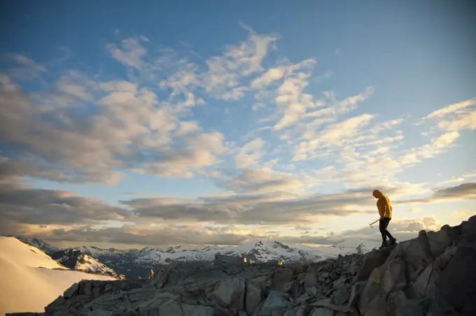Mountaineer holding ice axe navigates a rocky mountain ridge.