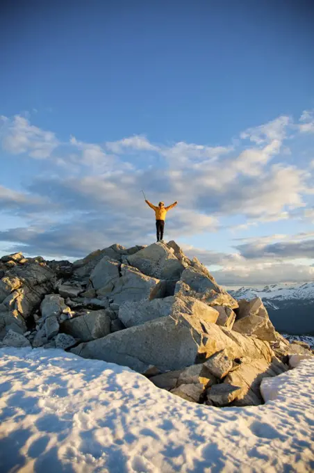Mountaineer raises arms after a successful climb to top of mountain.
