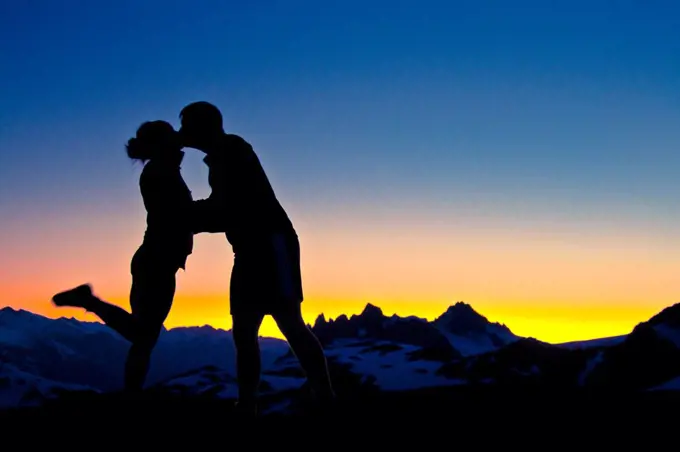 silhouetted Loving couple embrace and kiss on a mountain summit.