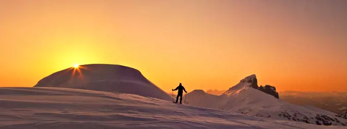 Panoramic view of explorer on snowy mountain ridge at sunset.