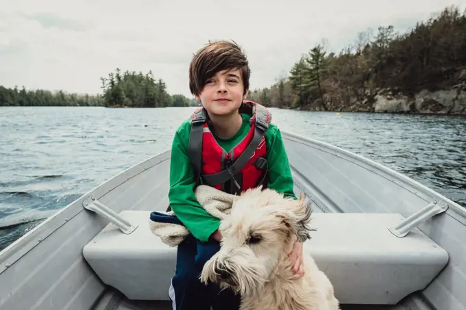 Young boy and dog sitting in a metal boat travelling on a lake.