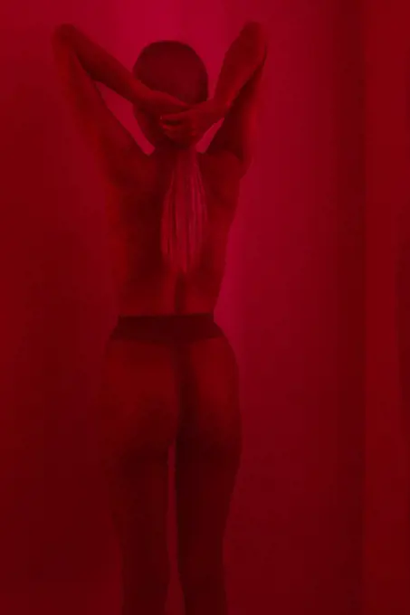Studio Fashion Portrait Of Blonde Wearing tights, back view, red filter.