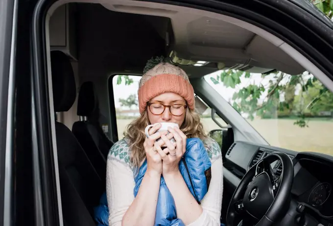 woman sat in a camper van enjoying a cup of coffee in a sleeping bag