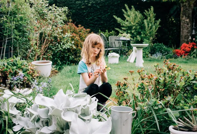 girl sat in a beautiful back yard picking flowers looking thoughtful