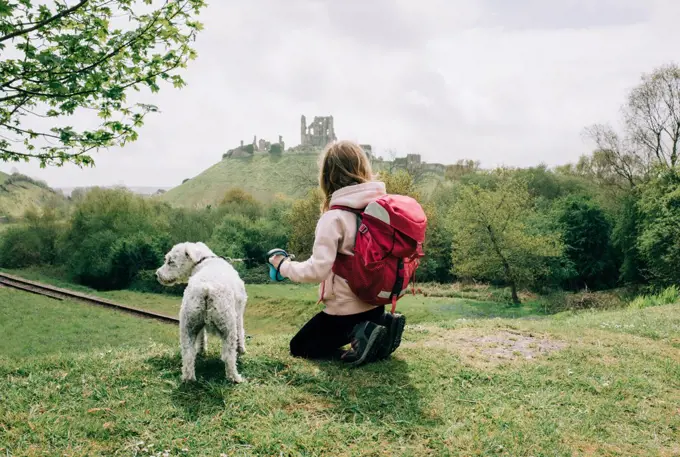 girl sat with her dog looking at a castle in the english countryside