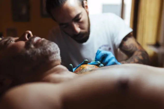 Front view of tattoo artist working with a customer in his studio.