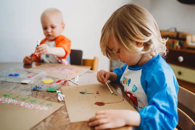 Young kids painting with lots of colorful paints at home in lockdown