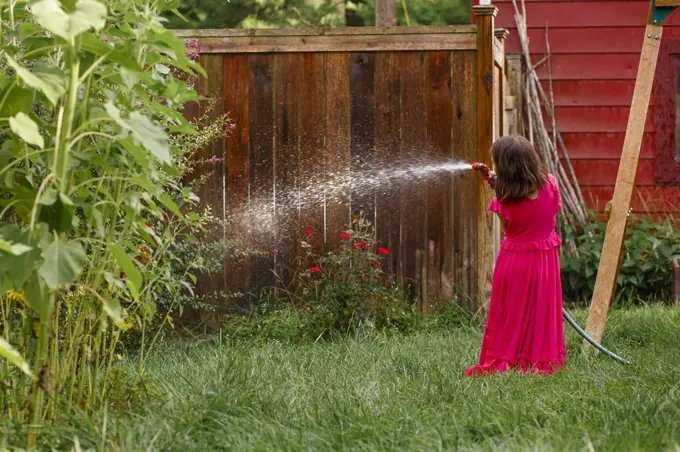 Rear-view of girl in long red dress watering roses in backyard garden