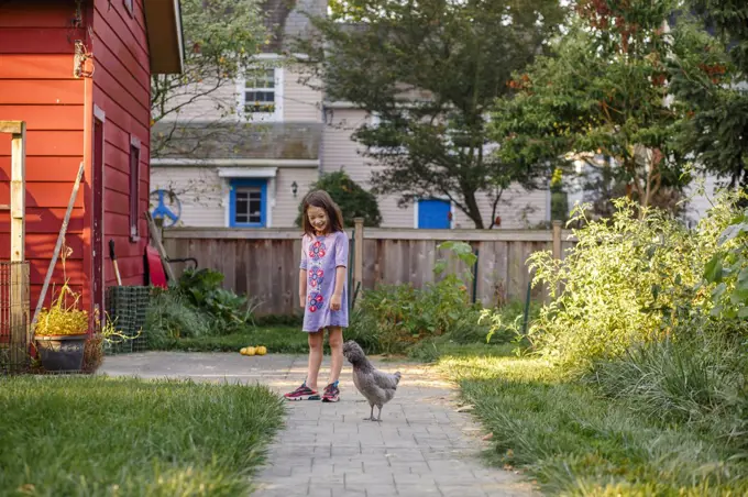 A smiling girl plays with her pet chicken outside in sunlit garden