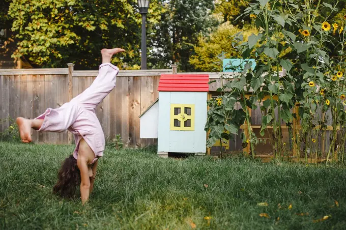 A little girl cartwheels in backyard by colorful chicken coop