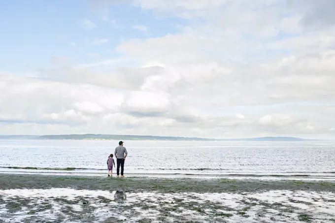 Wide view of a father and daughter standing together on a beach