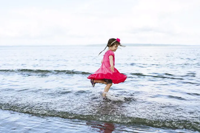 Side view of a young girl running through the shallow water at a beach