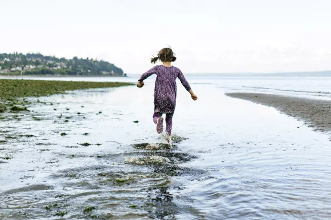 View from behind of a young girl running through shallow water