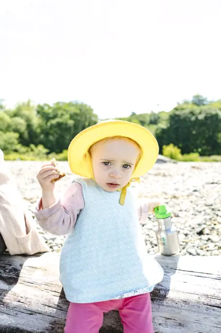 Portrait of a toddler in a sun hat eating lunch at the beach