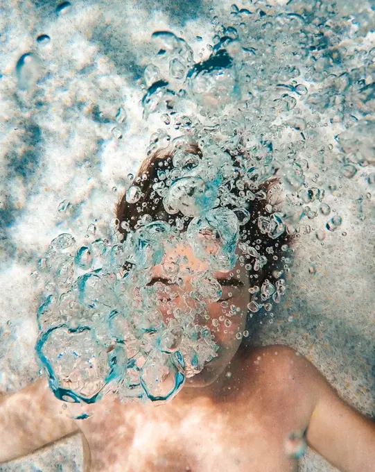Underwater image of teenage boy blowing bubbles in a pool.