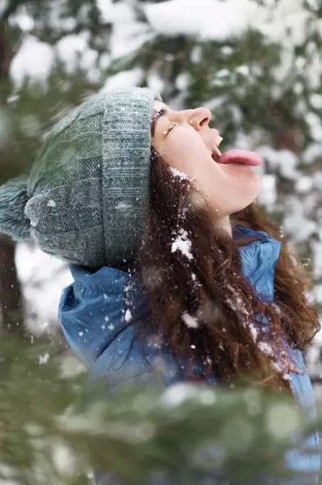 A young woman catches snow, sticking out her tongue, closes her eyes.