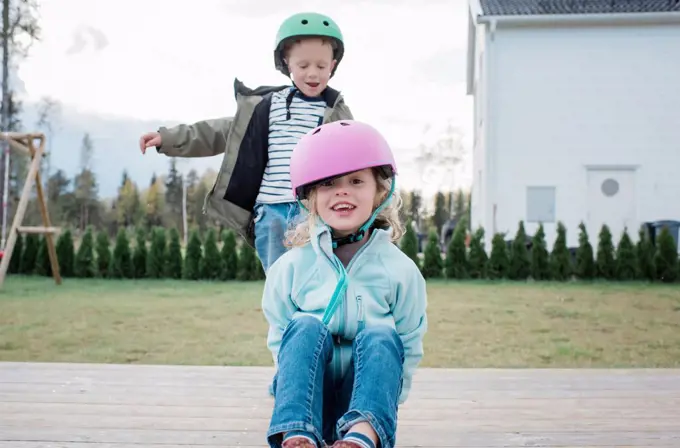 brother and sister playing on a skateboard in the garden laughing
