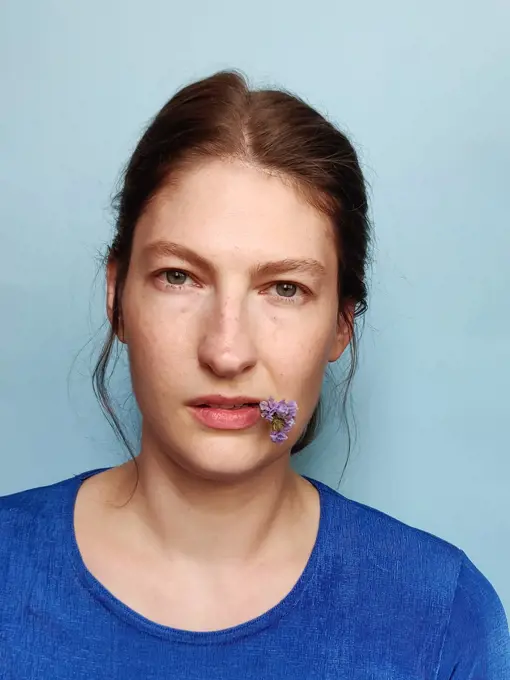 Portrait of a woman on a blue background holding a flower in lips