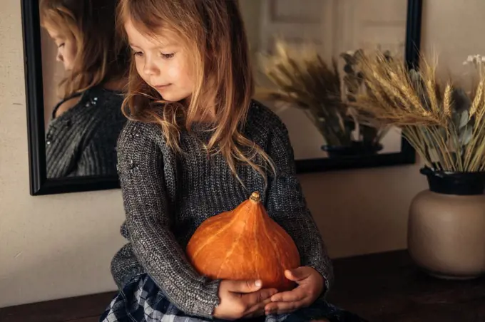 The cute girl holding a pumpkin in her hands sitting on the table.