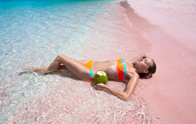 Girl Lays On Ombre Pink Sand & Turquoise Water Beach With Coconut