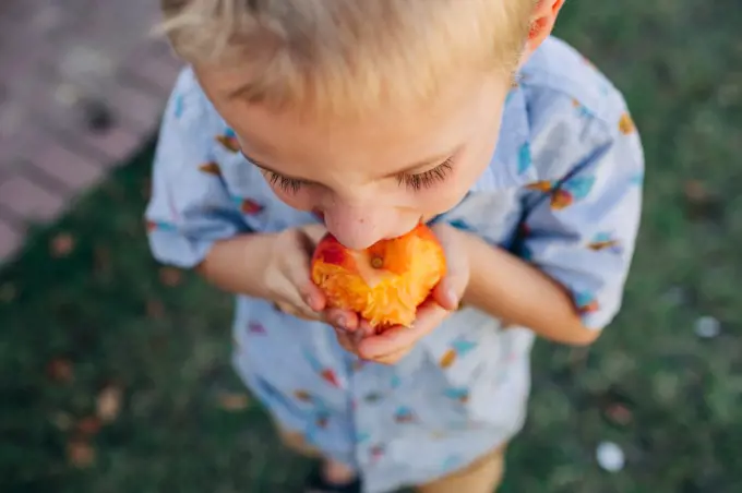 Close up shot of Caucasian boy eating peach in front yard